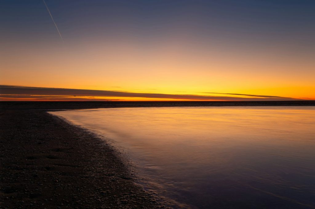 A seascape during sunset. Sand on the seashore. Bright sky during sunset.