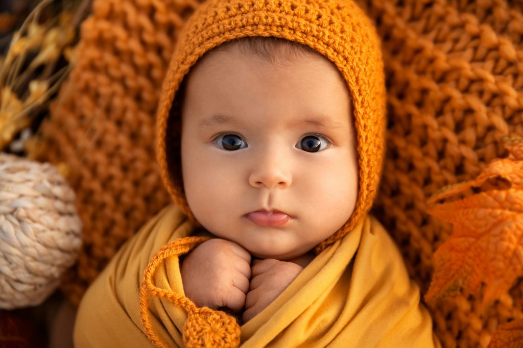 Autumn portrait of newborn baby girl swaddled in orange wrap