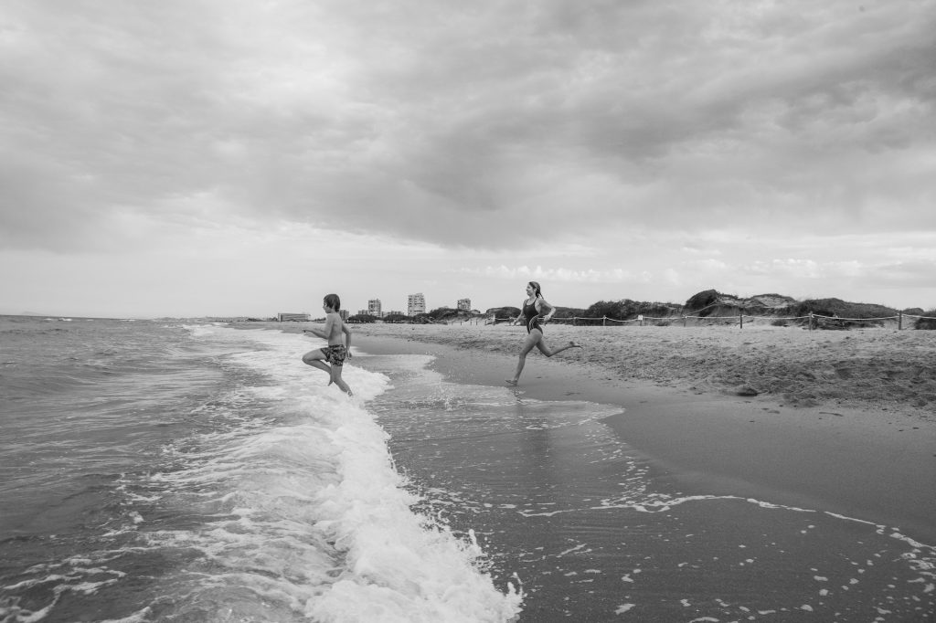 Black and white photography of a mother and her son on the beach running to bathe in the sea water.