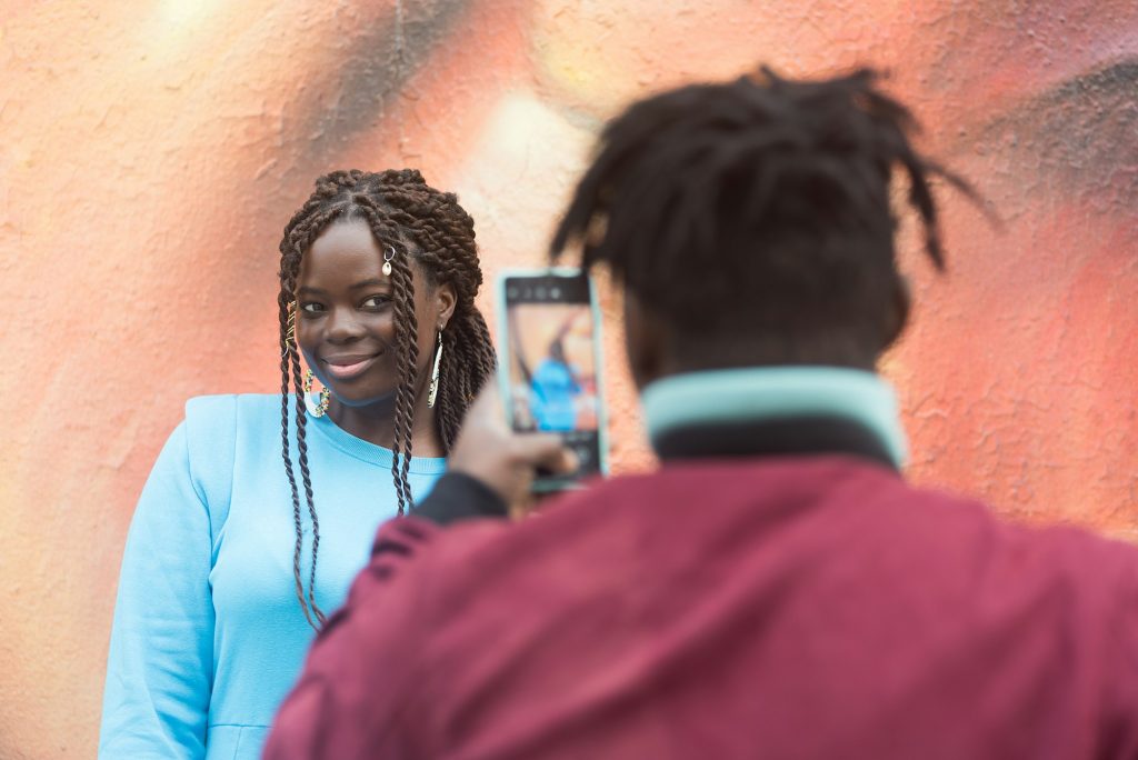 Black guy taking a photo with his mobile of his girlfriend.