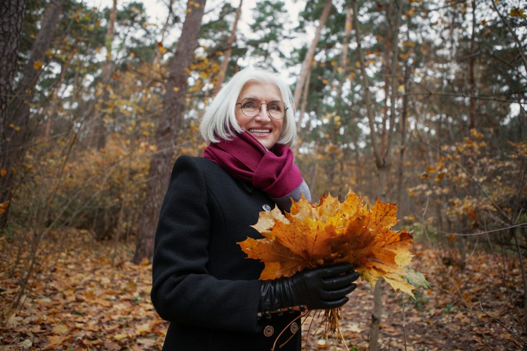 Caucasian happy senior woman with autumn leaves smiling in nature. Portrait active mature female