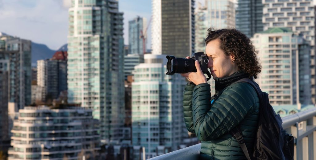 Caucasian Woman with camera taking images of modern cityscape. Travel photographer.