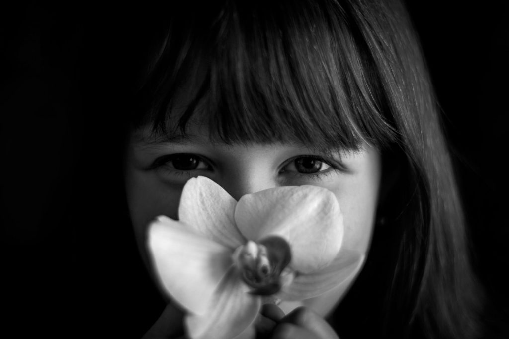 Close-up black and white portrait of adorable caucasian girl with orchid flower.