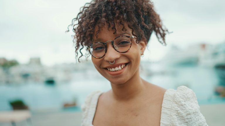 Closeup portrait of a young woman in glasses stands in the seaport and poses for the camera