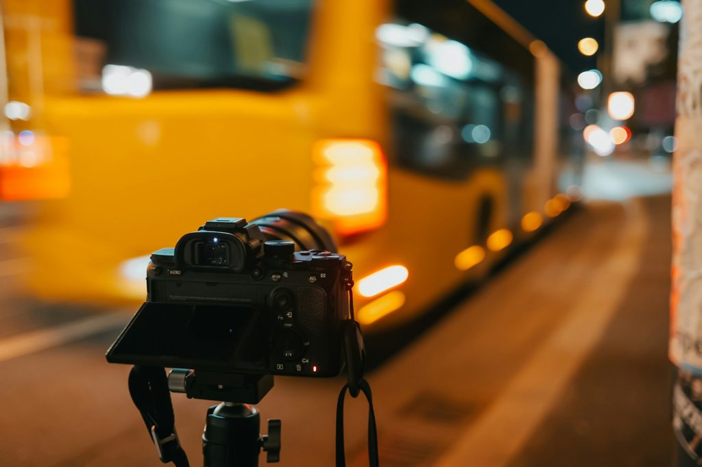 Digital modern camera filming a busy night street in big city. Yellow bus passes by. Photography cit