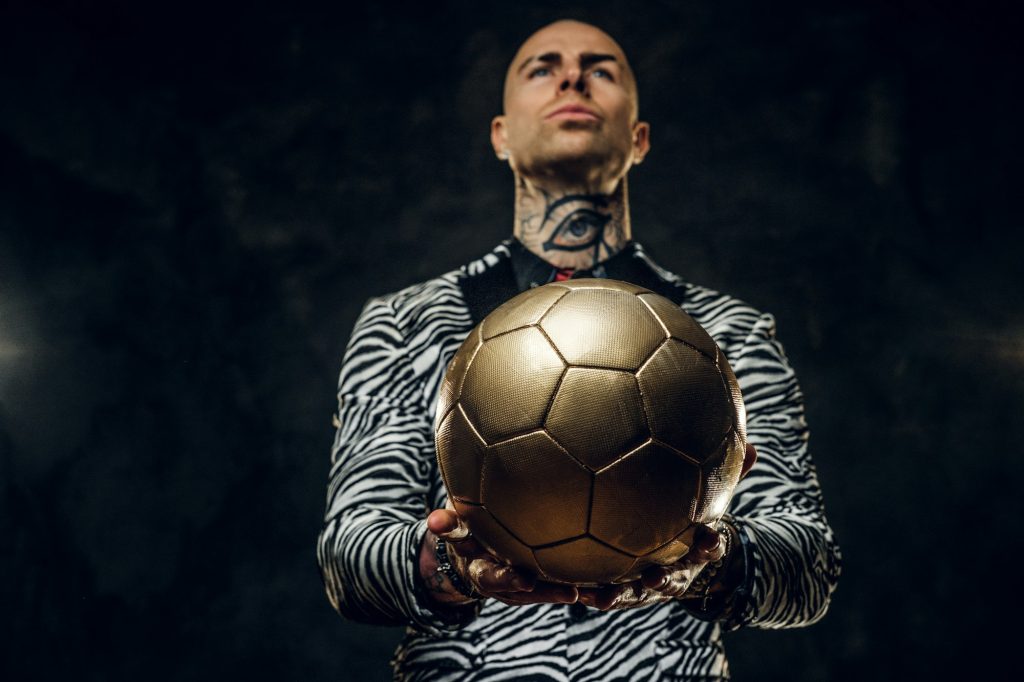 Elegant tattooed male model posing with a golden soccer ball in a studio