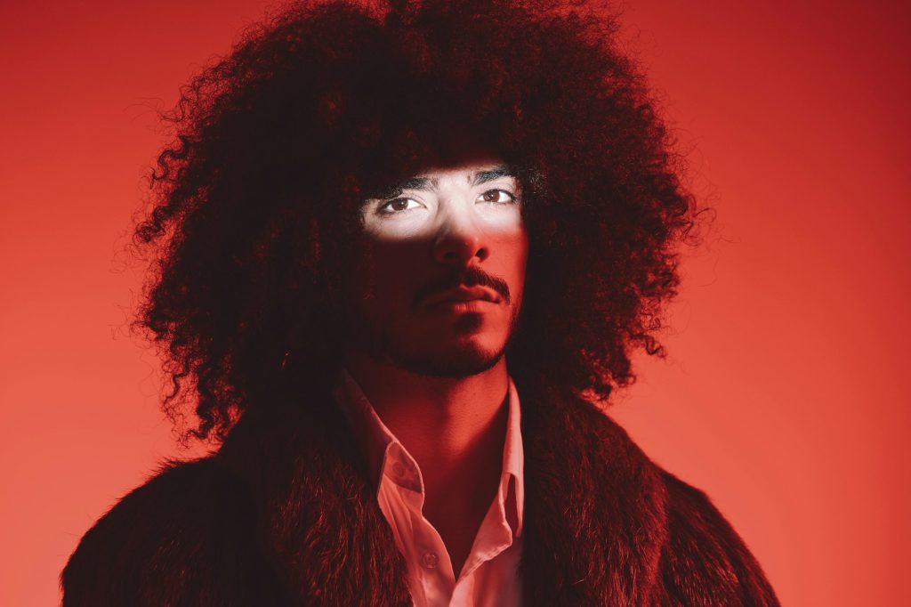 Fashion portrait of a man with curly hair on a red background, multinational, colored light, trendy