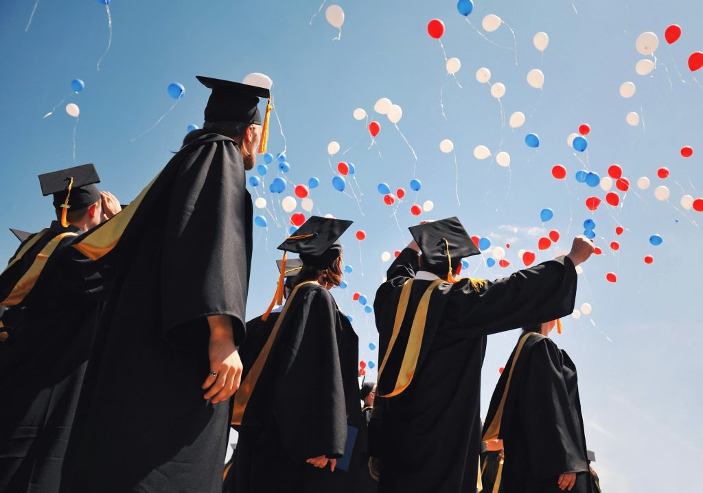 Graduates students in black robes rejoice against the blue sky