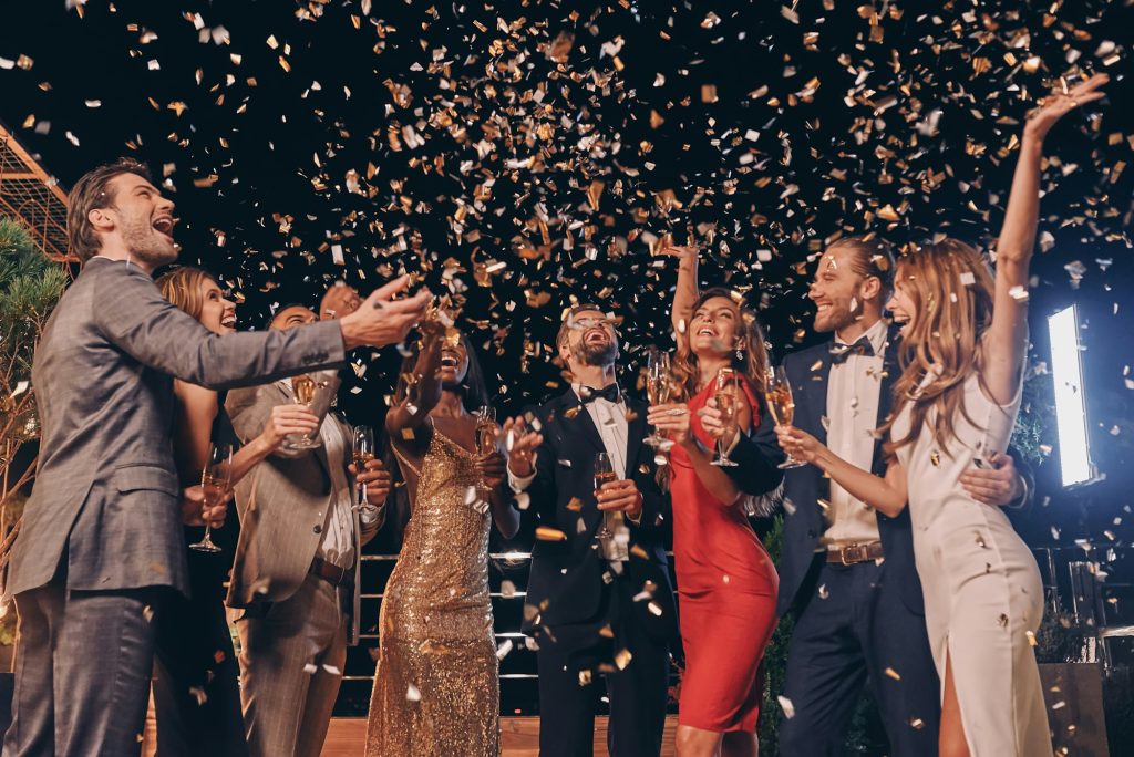 Group of beautiful people in formalwear having fun together with confetti flying all around