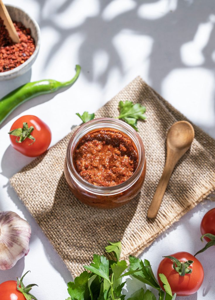 Homemade adjika sauce is an appetizer with tomatoes and hot peppers in a jar on a light background