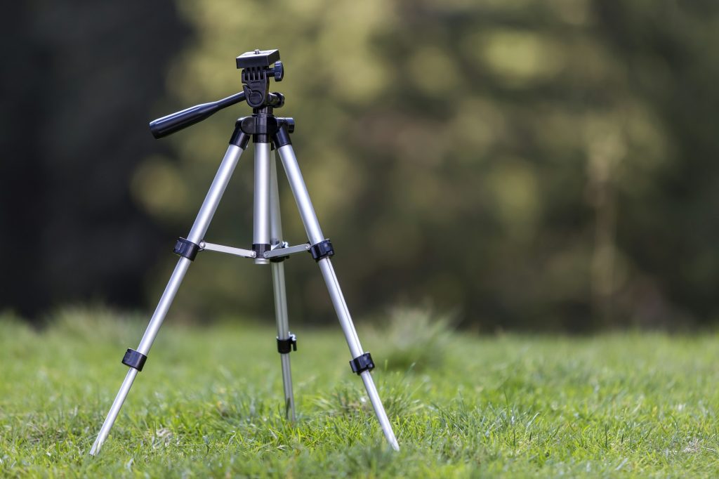 Isolated aluminum shiny tripod standing alone in fresh grassy meadow