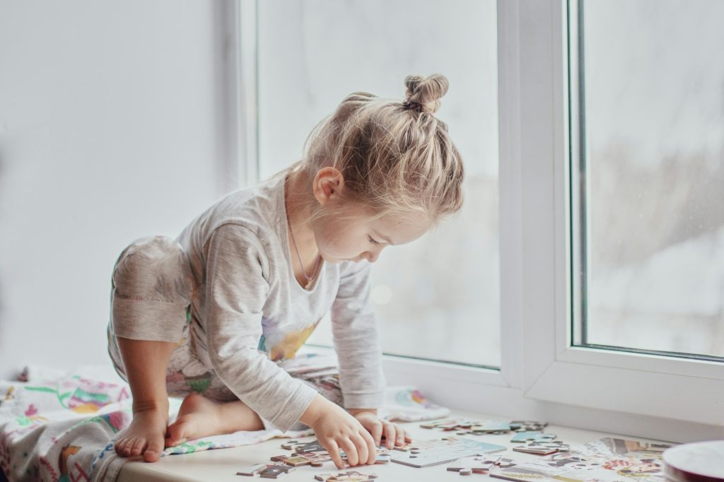 little girl collects puzzles by the window in light-colored hom