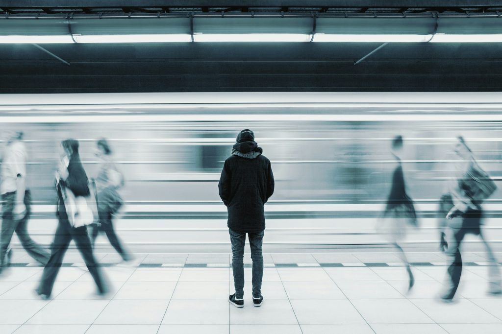 Long exposure picture with lonely man standing on station platform with blurry train and people