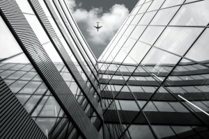 Low angle view of flying airplane over black and white modern architecture building