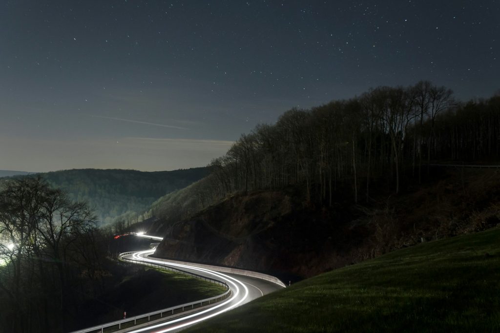 Night photo of the road with blurry car lights, visible hills and sky with stars