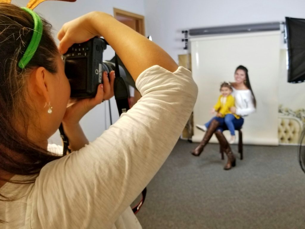 Photographer aiming the camera at an aunt and her niece during an indoor photo session