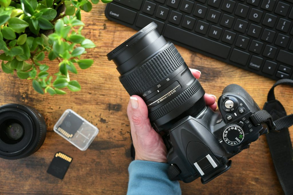 Photographer holding DSLR camera with zoom lens at desk with SD cards and computer keyboard