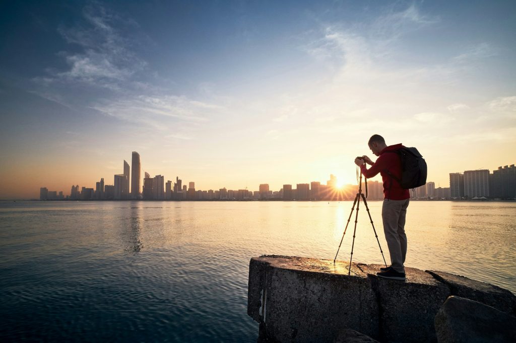 Photographer with camera on tripod photographing urban skyline at sunrise