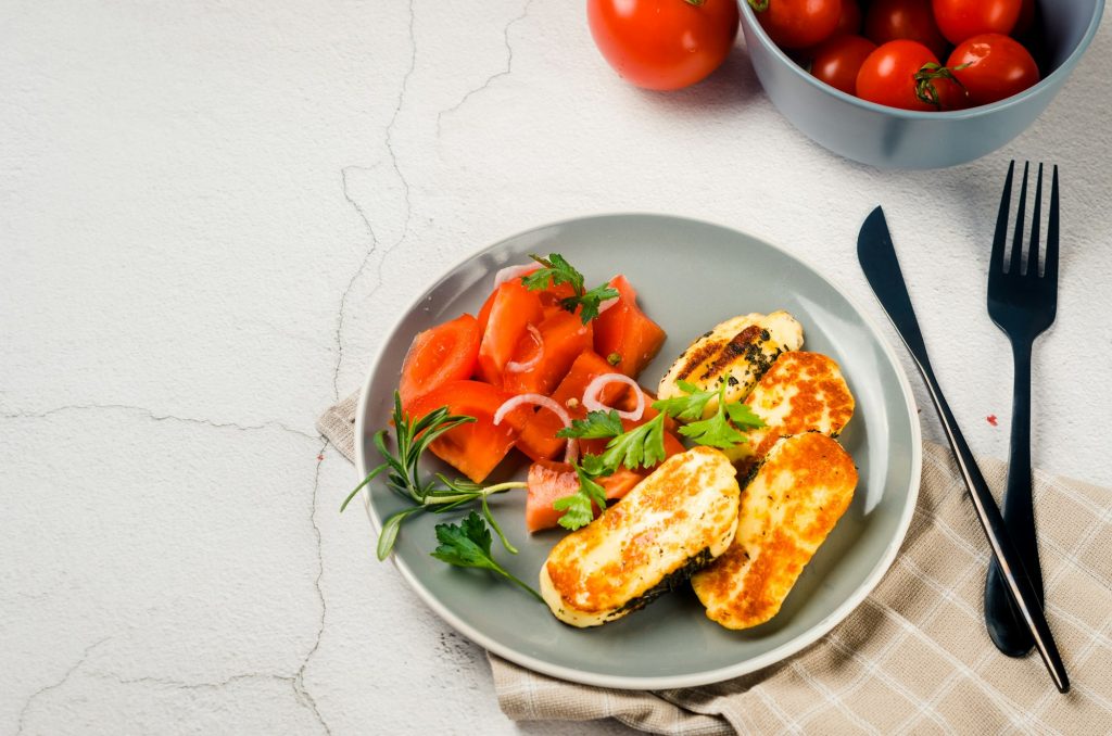 Pieces of fried halloumi on a plate and tomatoes. Balanced and healthy food.