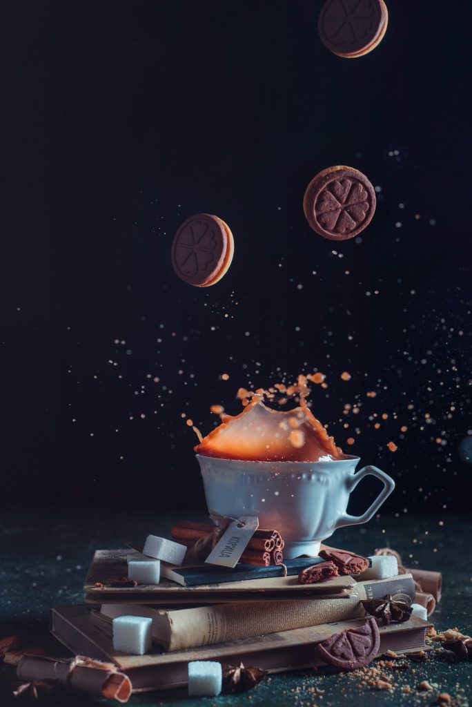 Porcelain tea cup with falling cookies and a splash on a dark background. Frozen motion food