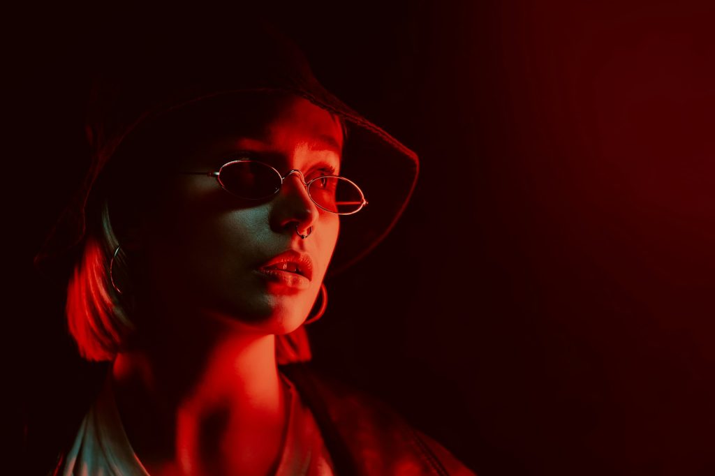 Portrait if stylish woman in dark studio under red neon. Panama, round eyewear