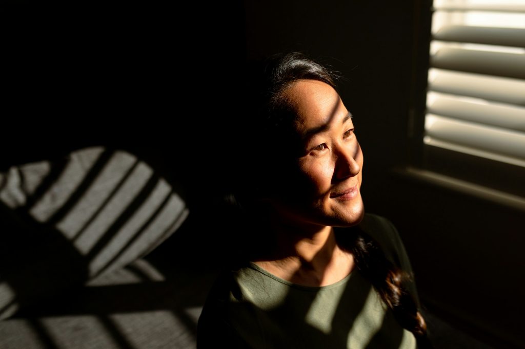 Portrait of happy asian woman standing in ray of light at window