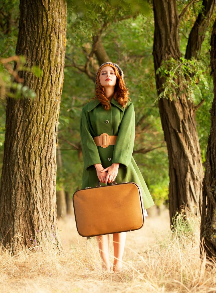 Redhead girl with suitcase at tree's alley.