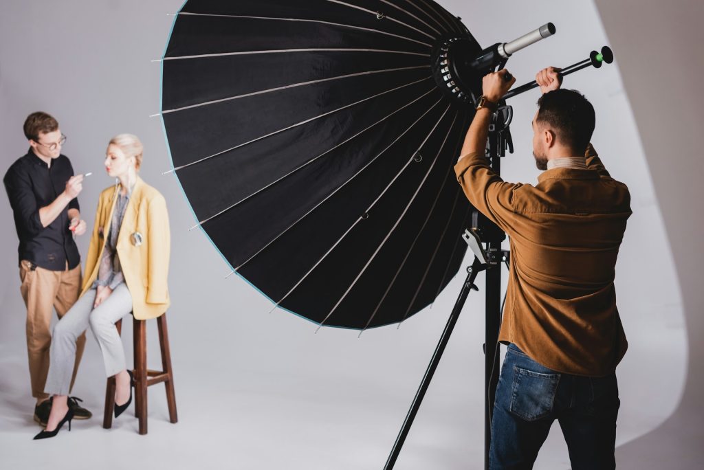 selective focus of photographer touching reflector on backstage and Makeup Artist doing makeup to