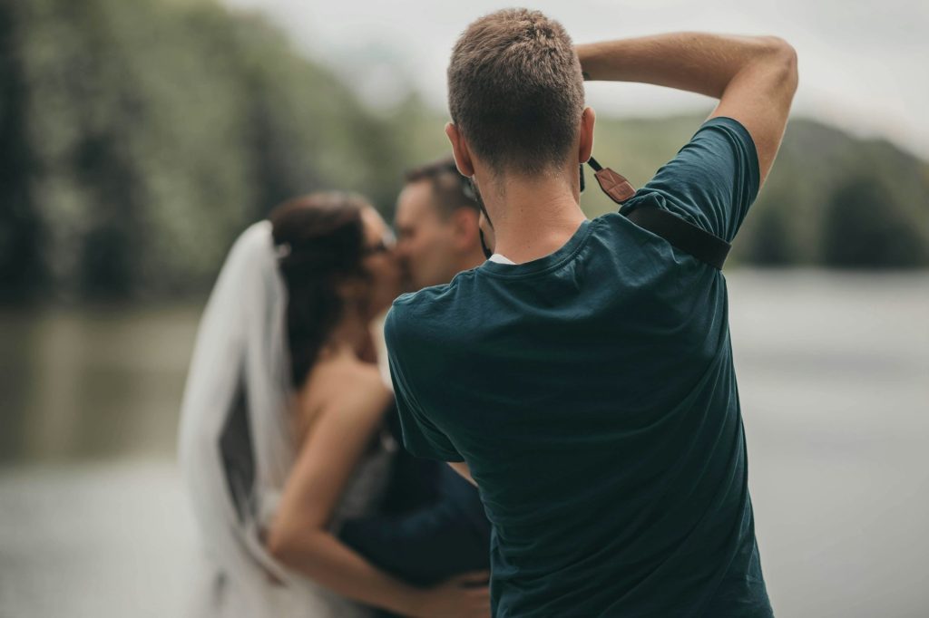 Shallow focus of a male photographer taking pictures of a newly married kissing couple