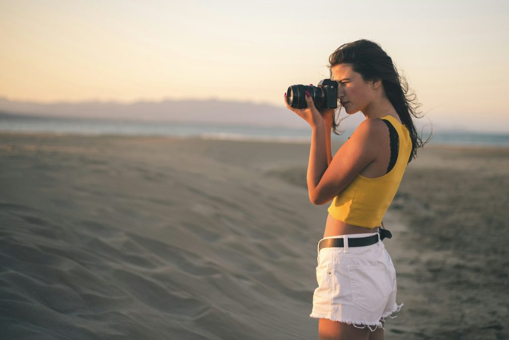 Teenage girl taking photos with camera on the beach at sunset