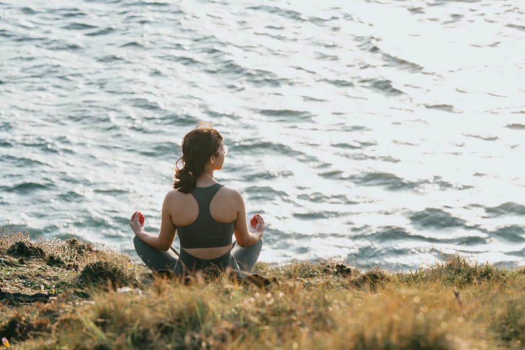 Young fit woman doing yoga in the rocks of a wild coast with the ocean in front during a sunny day