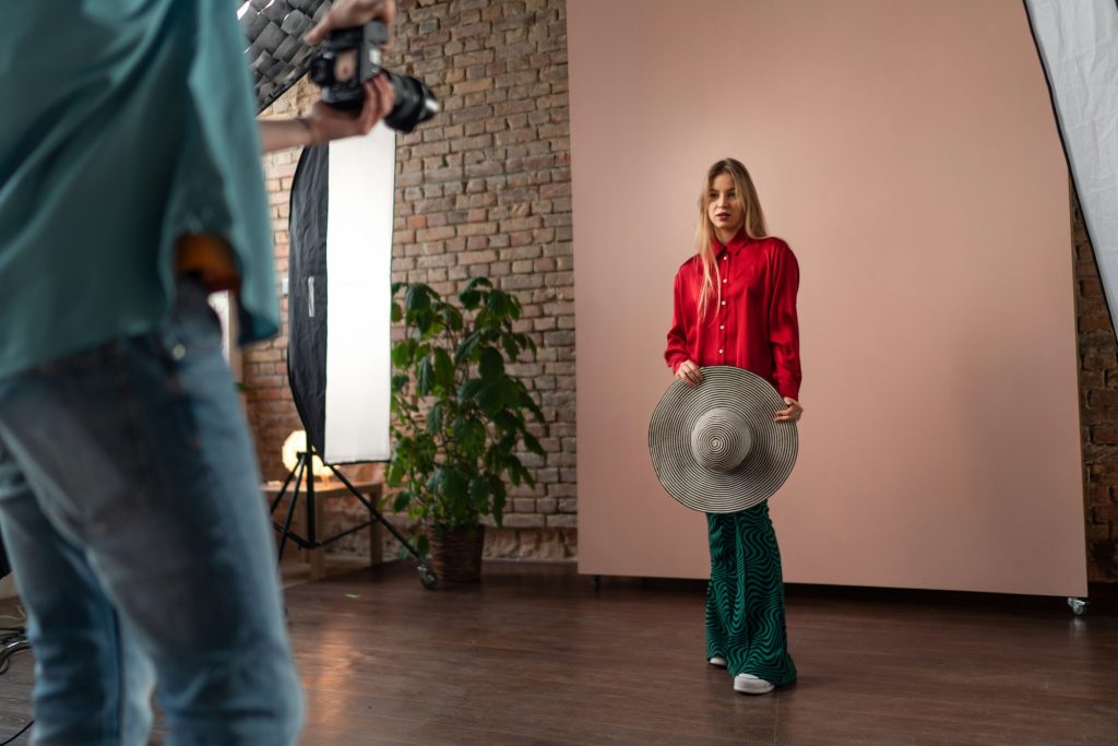 Young photographer taking picures of model, backstage of photoshooting in studio.